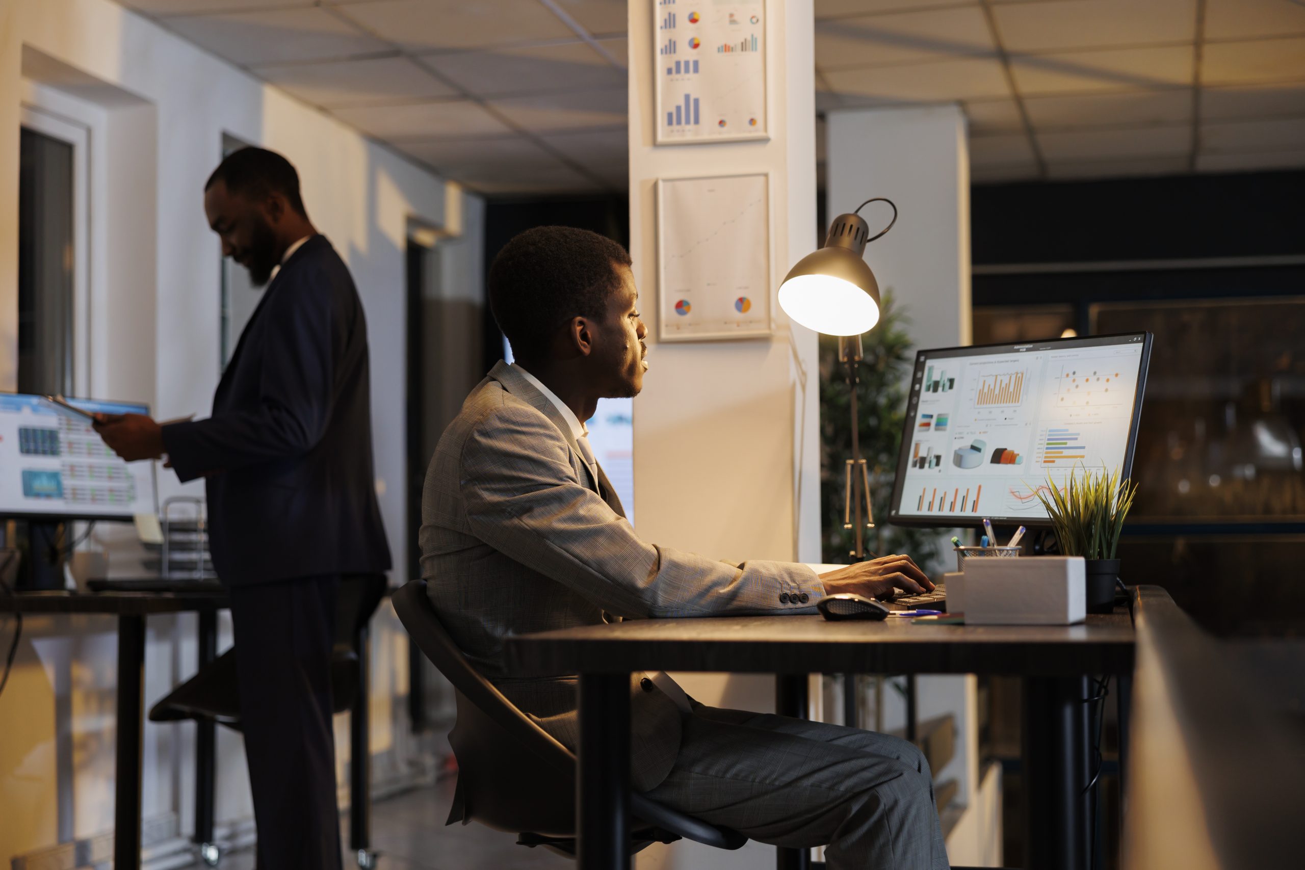 African american businessman looking at financial graphs report on computer, planning company investment typing business strategy. Executive manager working late at night in startup office